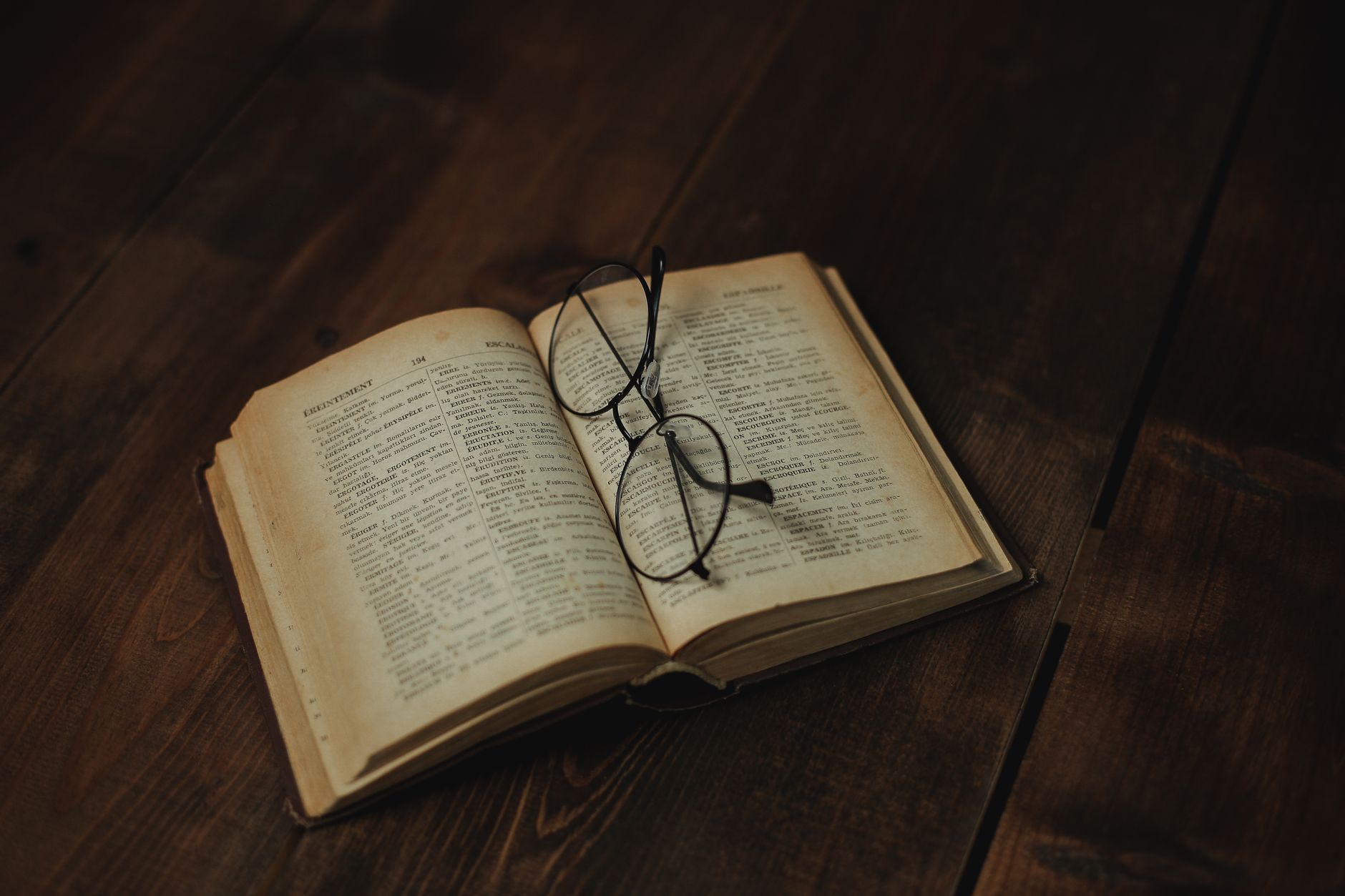 Open vintage book with eyeglasses resting on a wooden surface, evoking a sense of nostalgia
